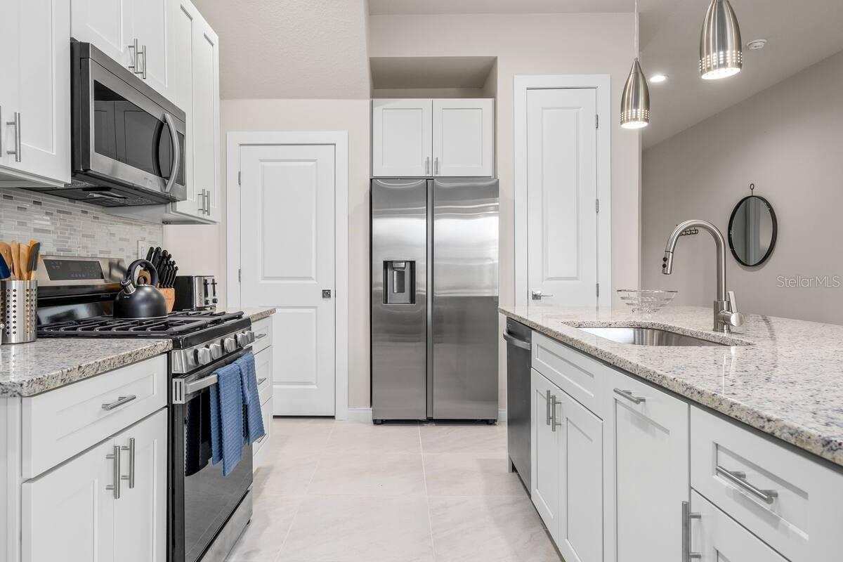Modern kitchen with white cabinets, stainless steel appliances, and a granite island with sink.