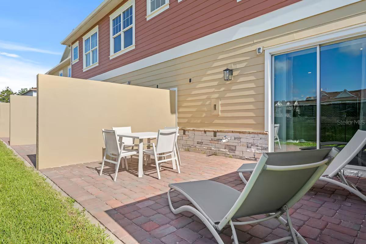 Paved home patio with outdoor dining set, reclining loungers, and a tall privacy wall.