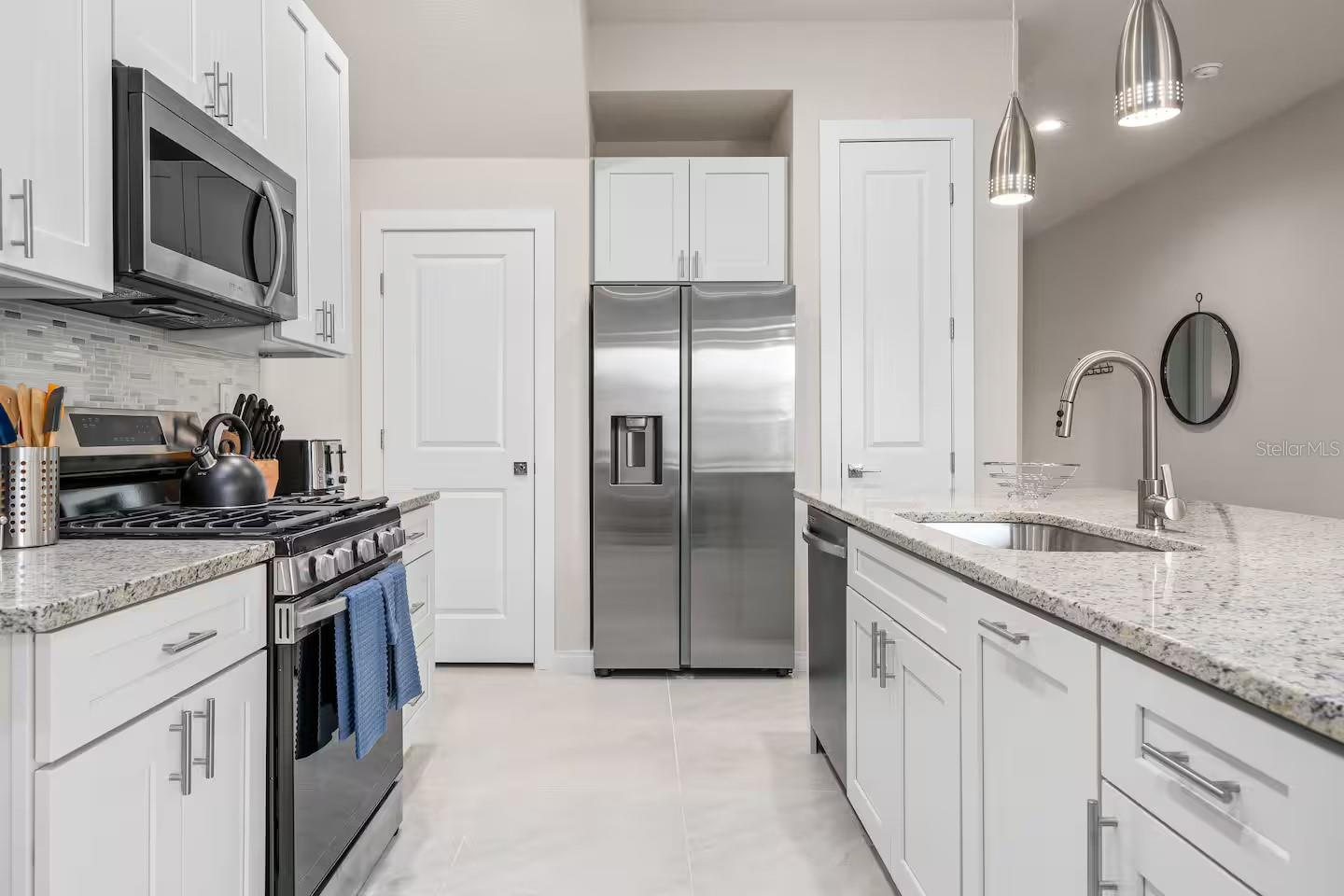 Modern white kitchen with stainless steel appliances, speckled stone counters, and a peninsula sink.
