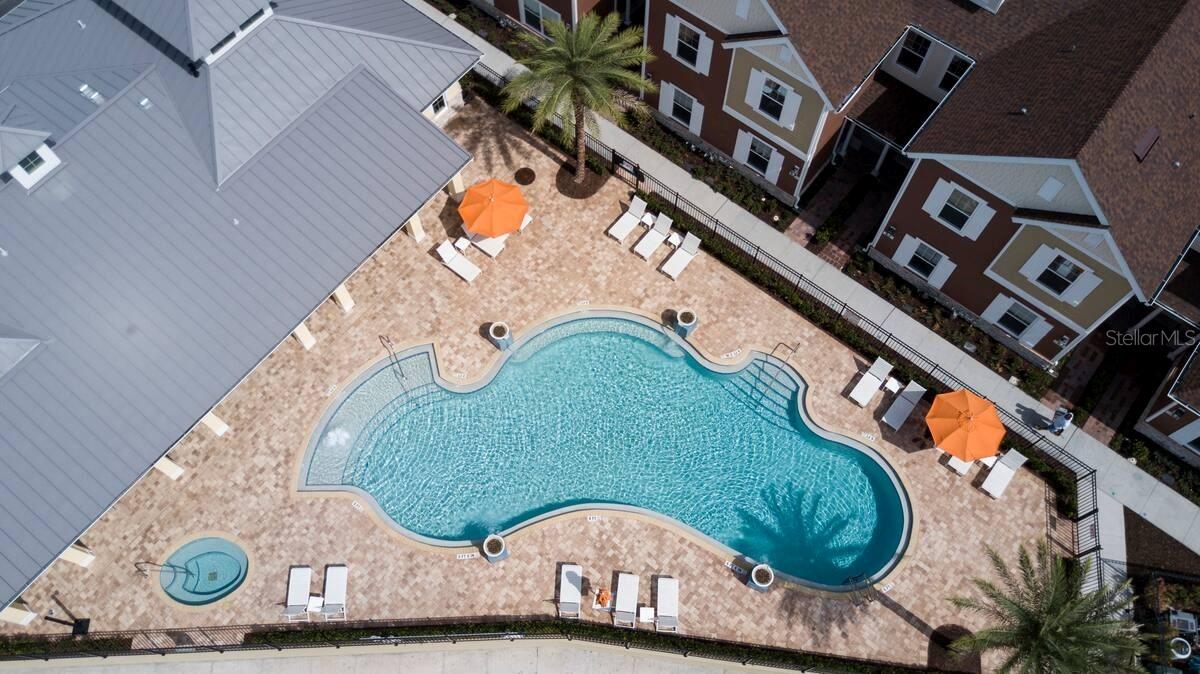 Freeform swimming pool with orange umbrellas and lounge chairs on a paved courtyard.