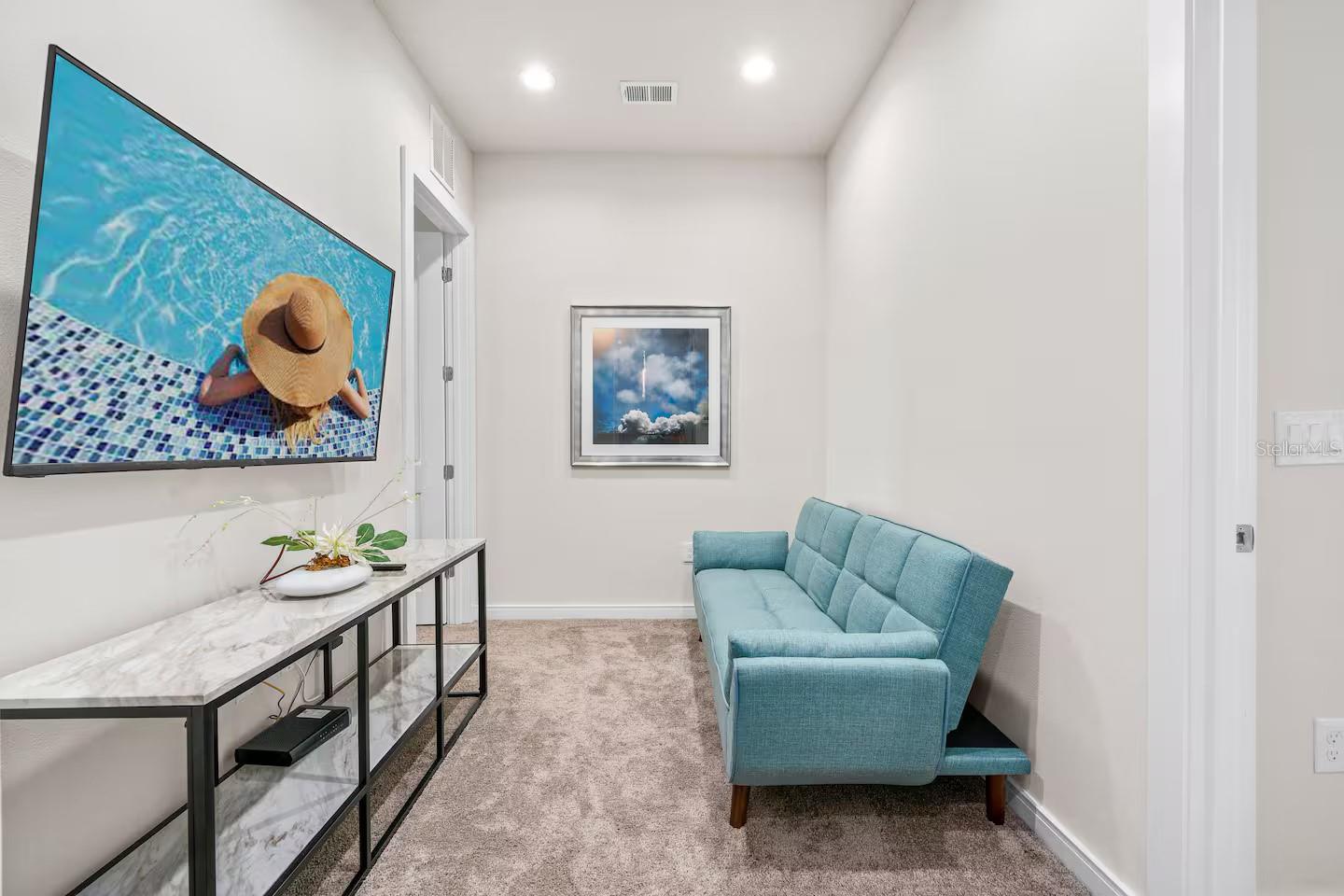 Media room with a turquoise sofa, wall-mounted television, and marble-look console.