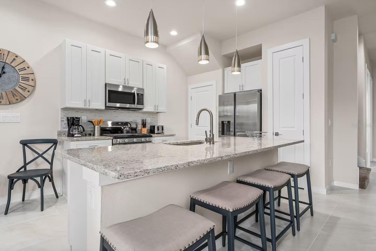 Kitchen with a large speckled stone island, four stools, white cabinets, and stainless steel appliances.