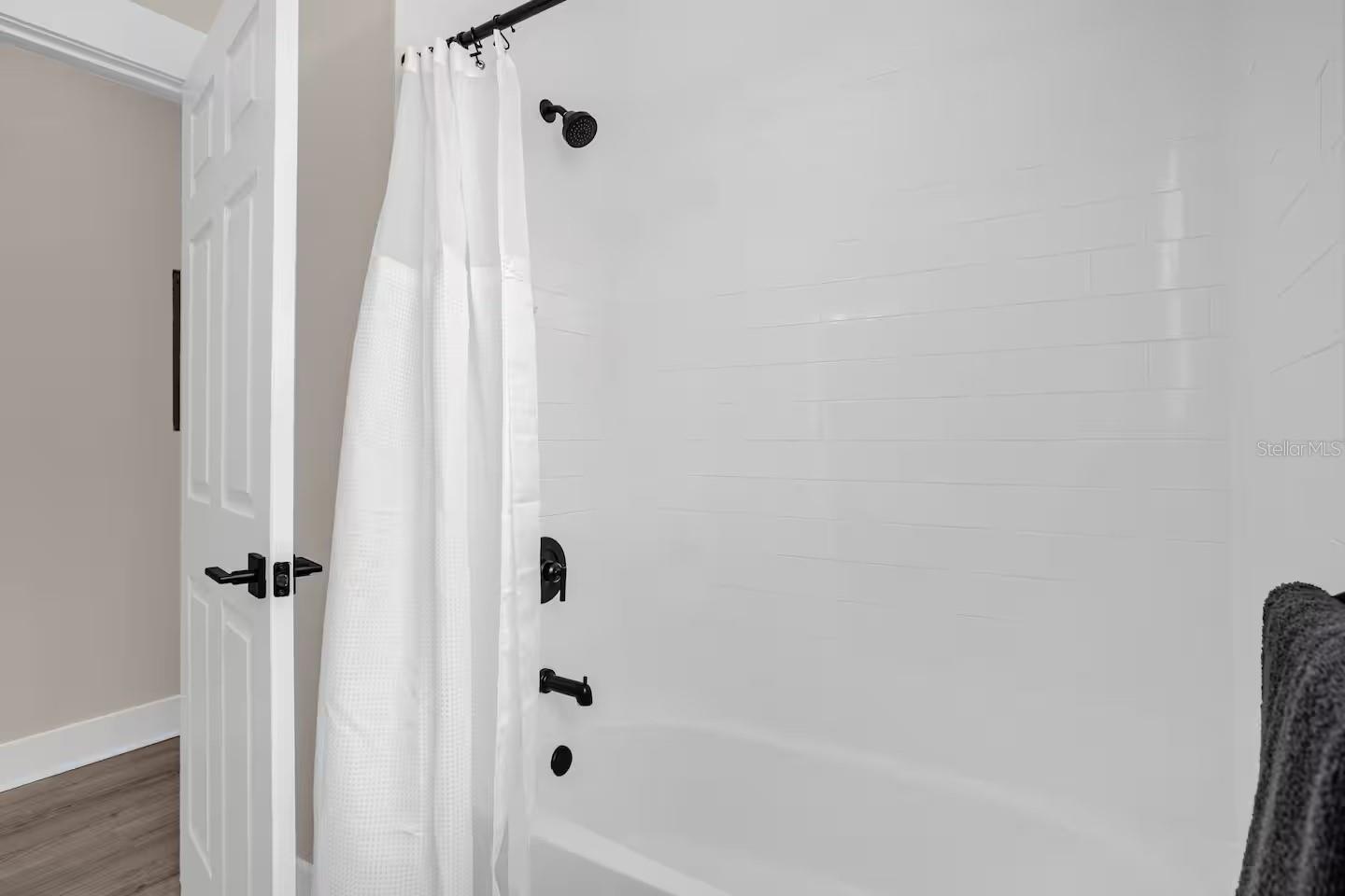 Bathroom with a white tiled tub and shower, black fixtures, and a white curtain.