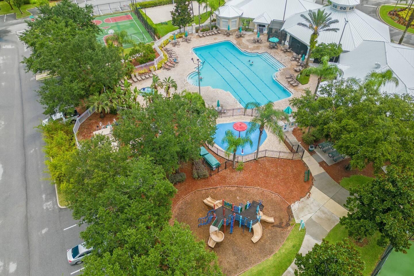 Aerial view of a community pool, splash pad, playground, tennis courts, and clubhouse.