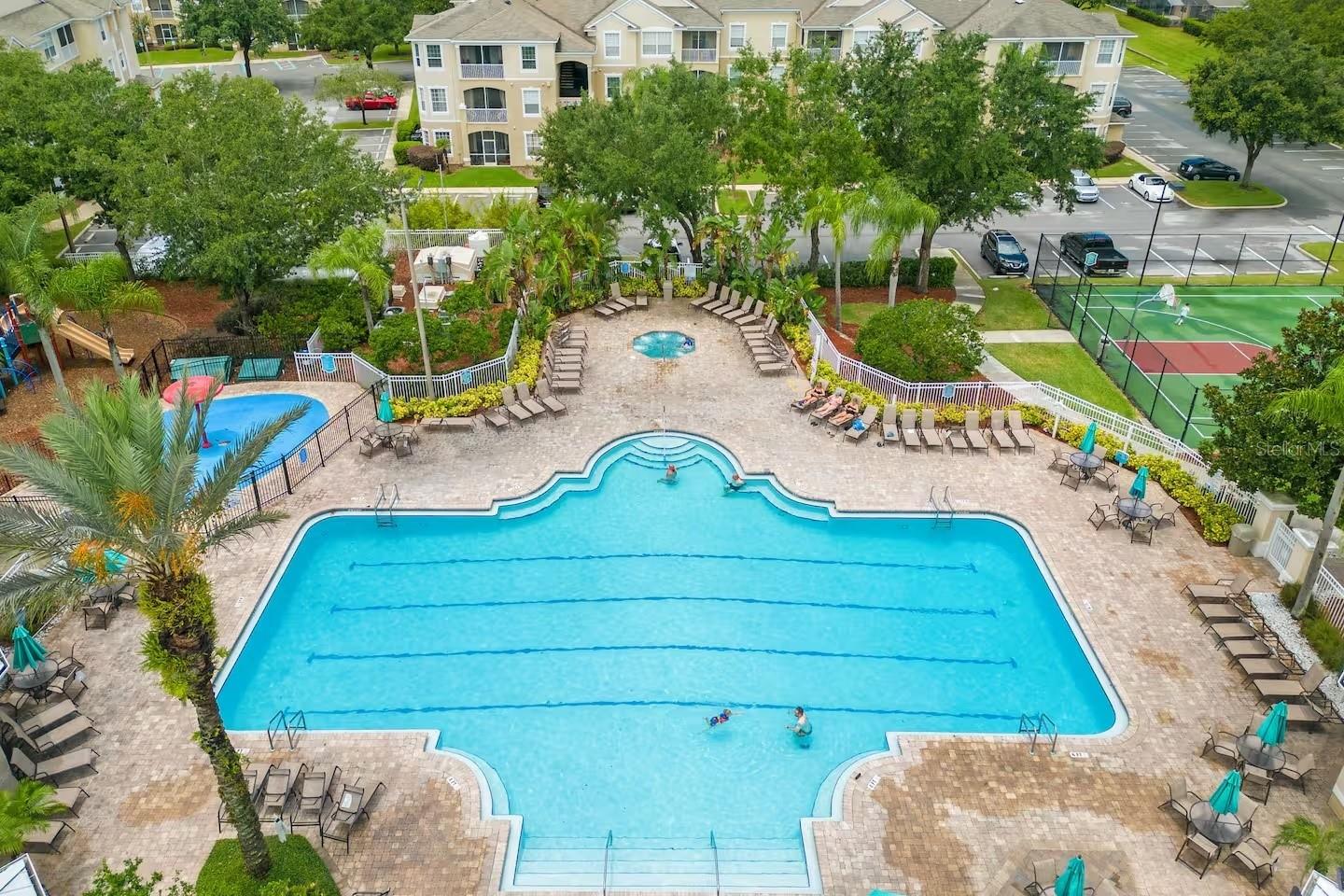 Aerial view of a large community swimming pool beside a smaller pool and fenced tennis court.