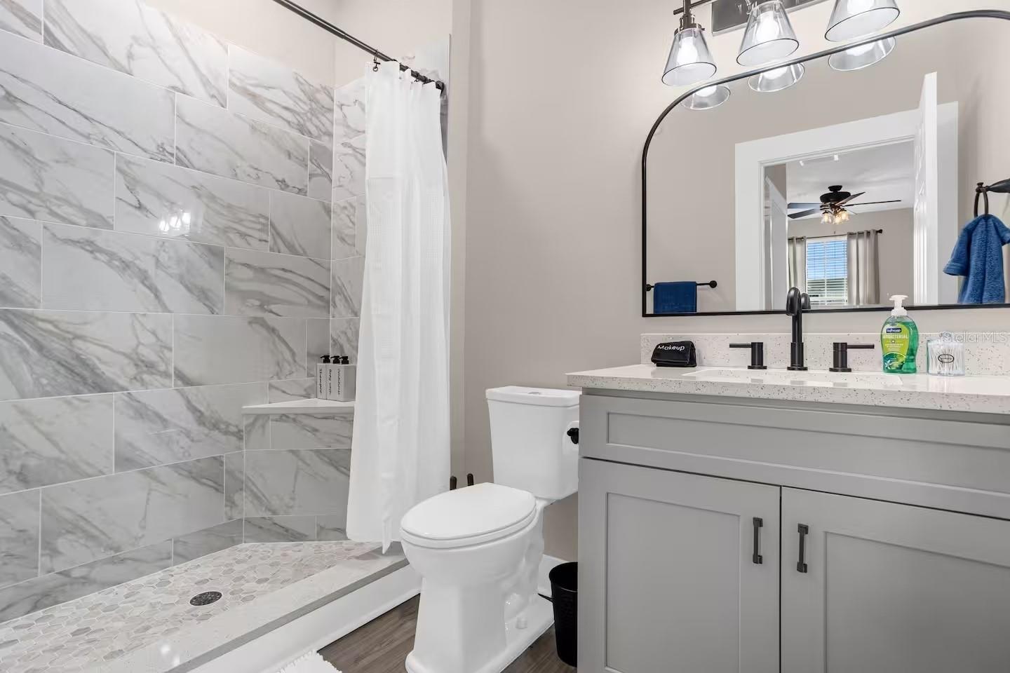 Updated bathroom with marble-look shower tile, gray vanity, speckled countertop, and arched mirror.