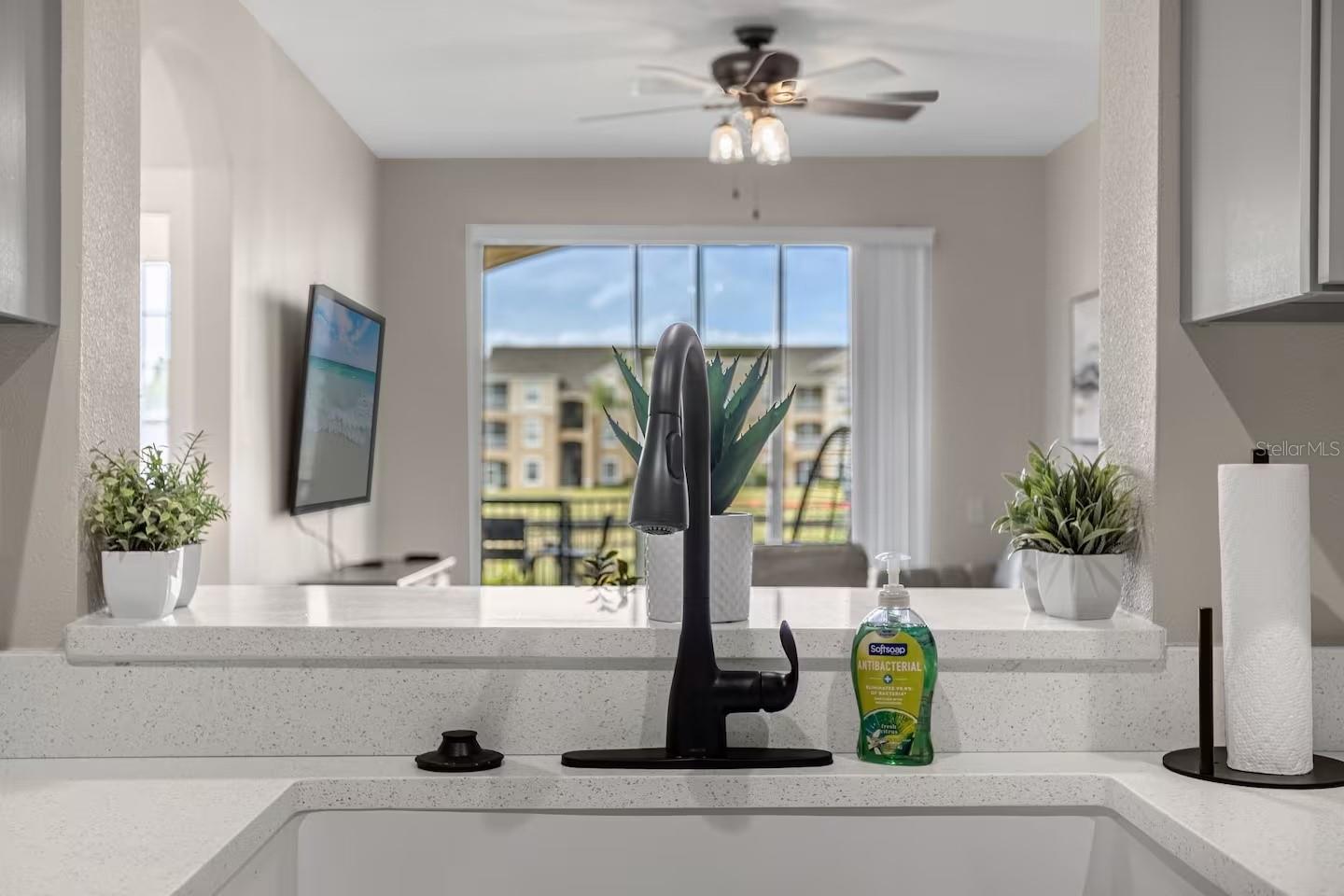 Kitchen sink with a black faucet and quartz counter overlooking the living area and balcony.