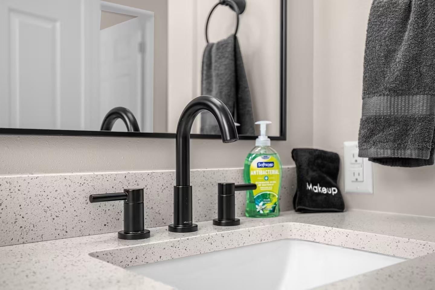Bathroom vanity with a speckled countertop, matte black faucet, and gray towels.