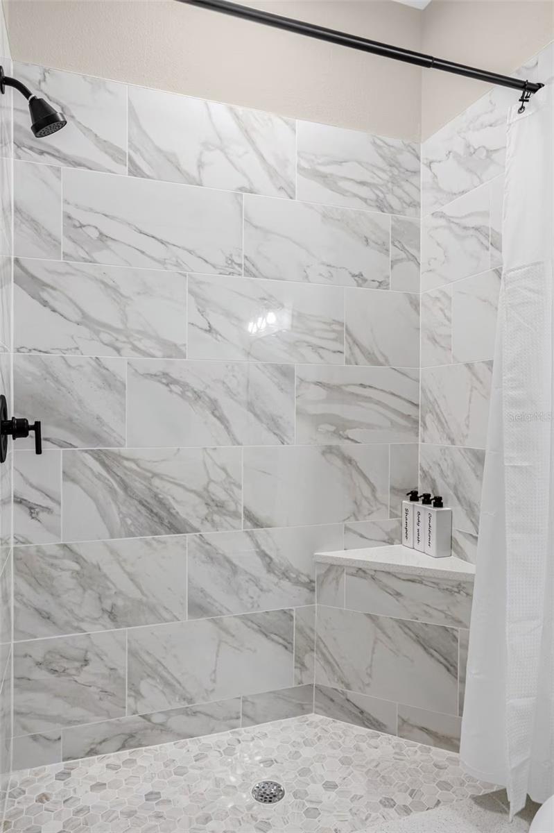 Walk-in shower with marble-look tile walls, a hexagonal mosaic floor, and black fixtures.