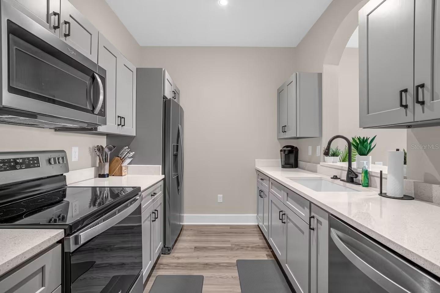Galley kitchen with gray cabinets, white counters, and stainless steel appliances.