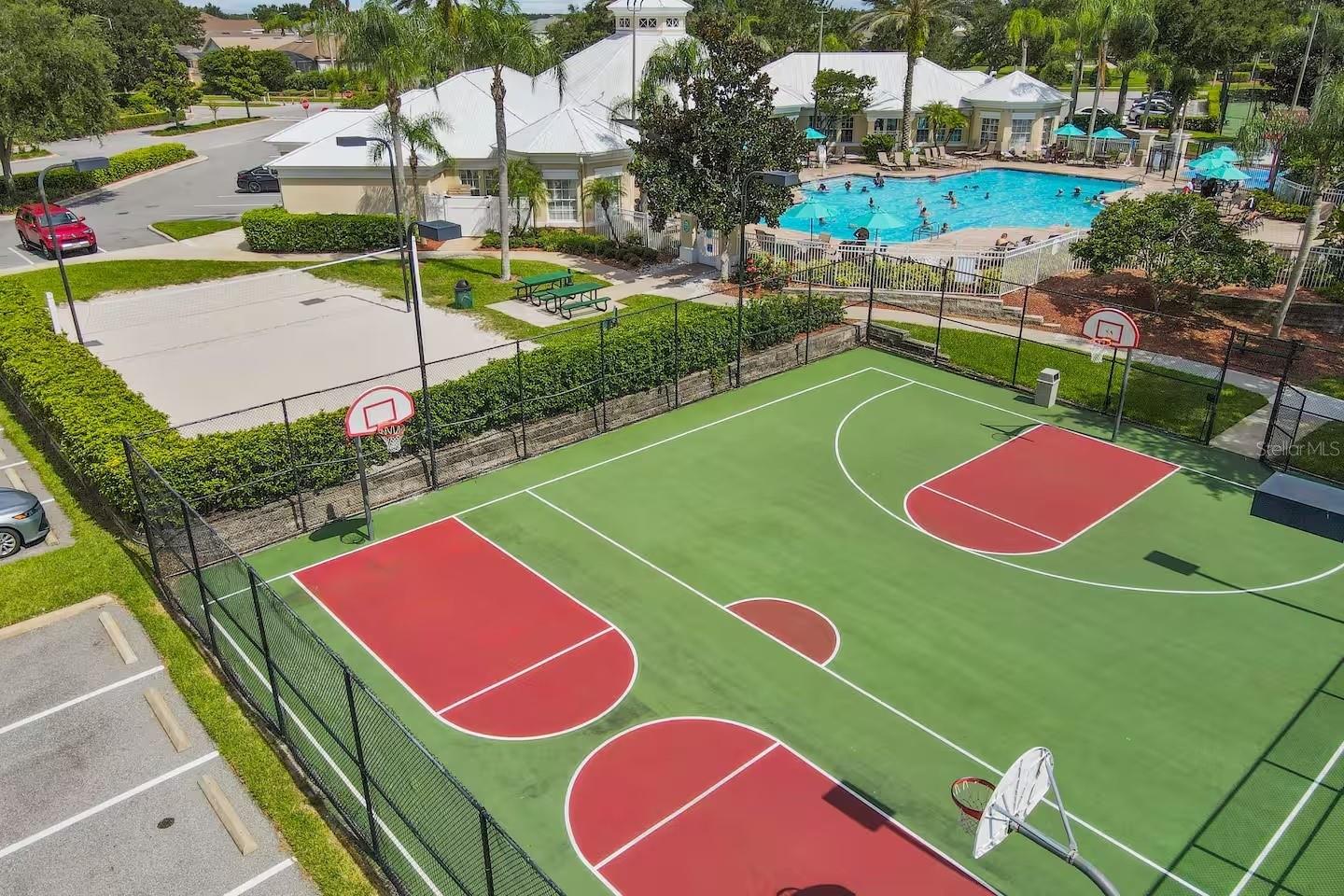 Aerial view of a fenced basketball court beside a community pool and clubhouse.