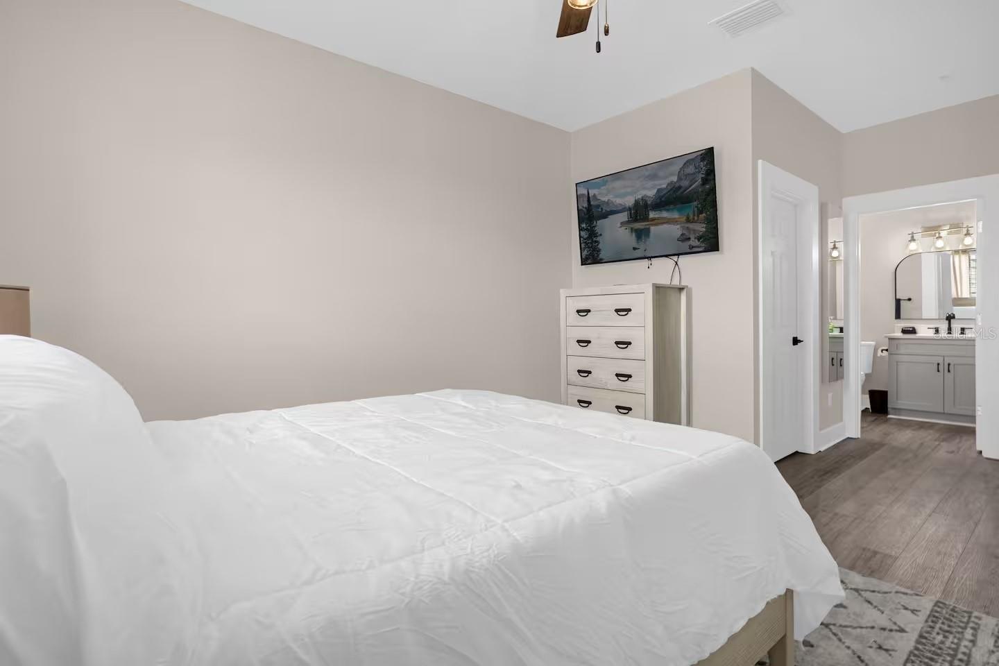 Furnished bedroom with a white bed and dresser, opening to a bathroom with a vanity.