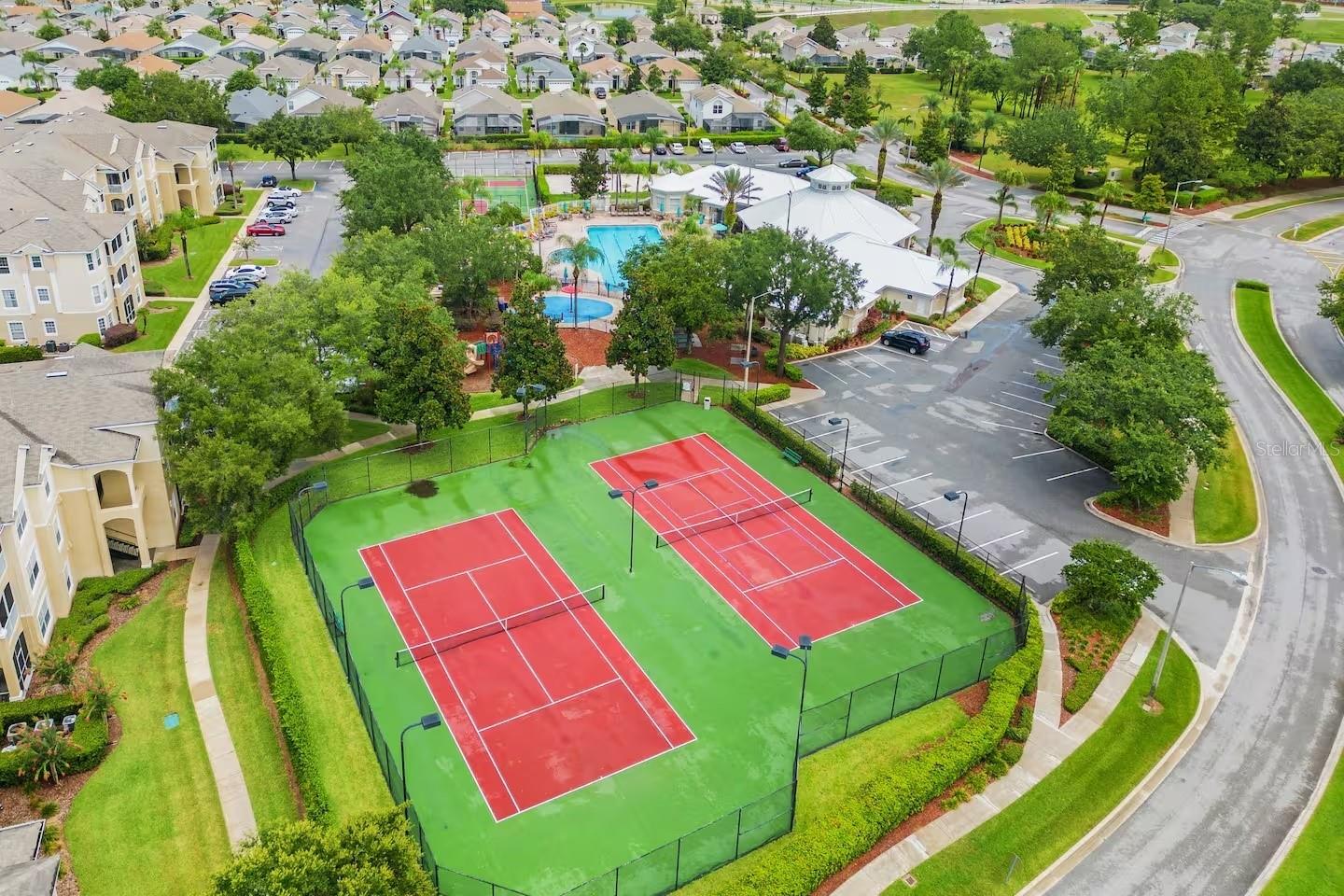 Aerial view of community tennis courts beside a swimming pool and clubhouse.