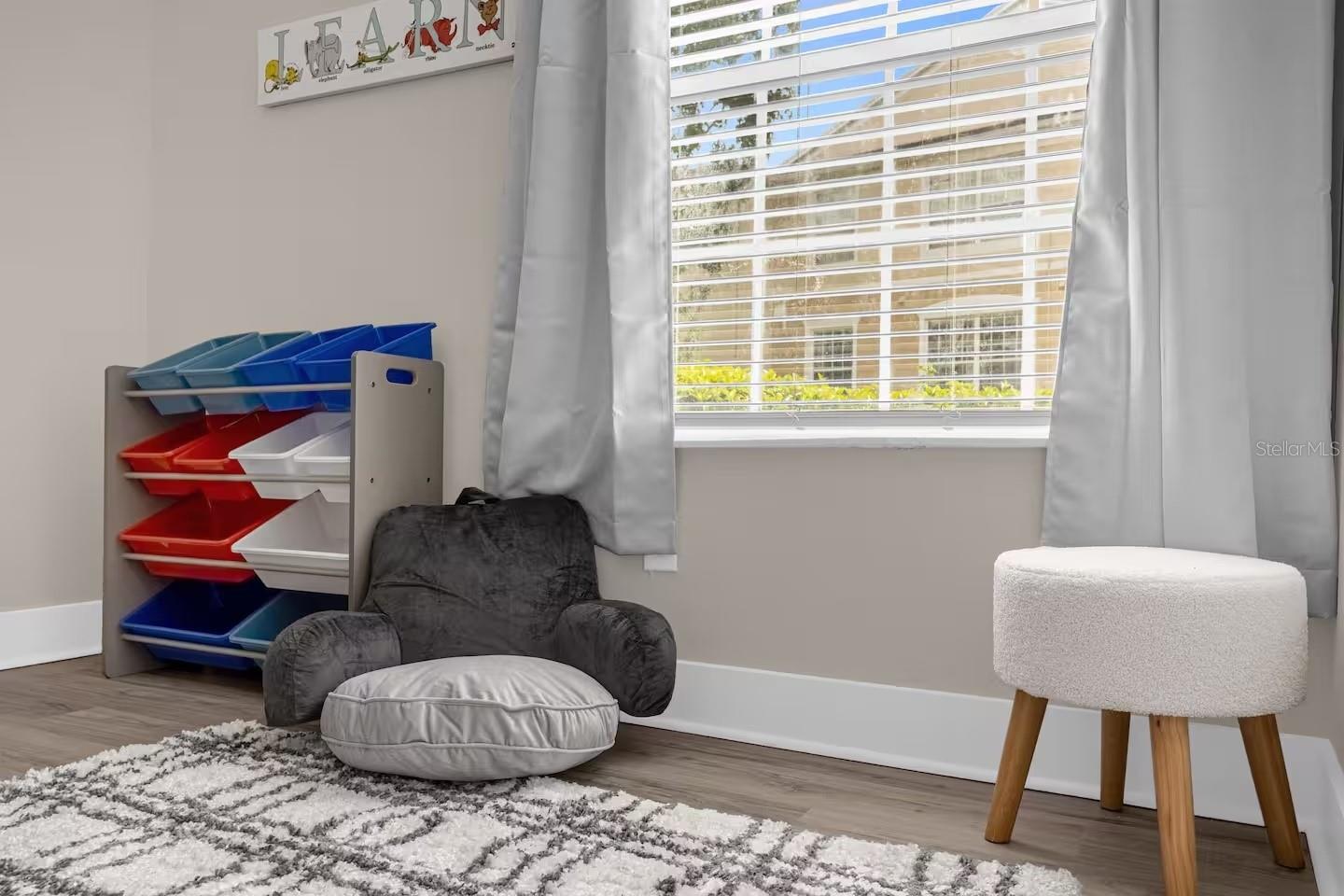 Children’s playroom with colorful toy bins, a gray floor chair, and a bright window.