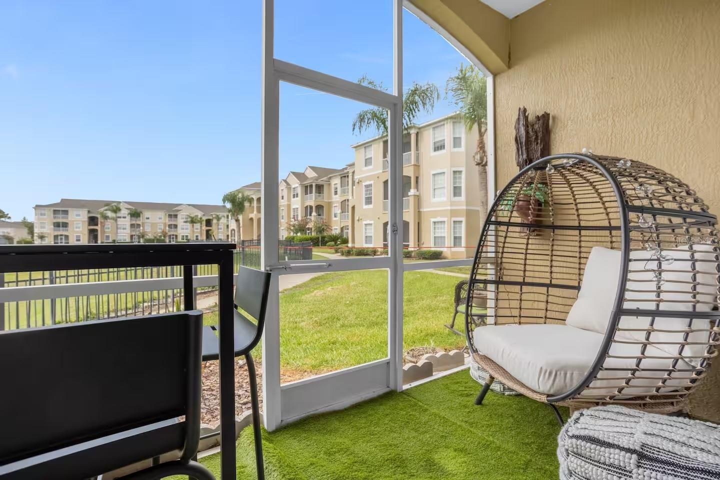 Screened patio with artificial turf and a hanging egg chair overlooking landscaped apartment grounds.