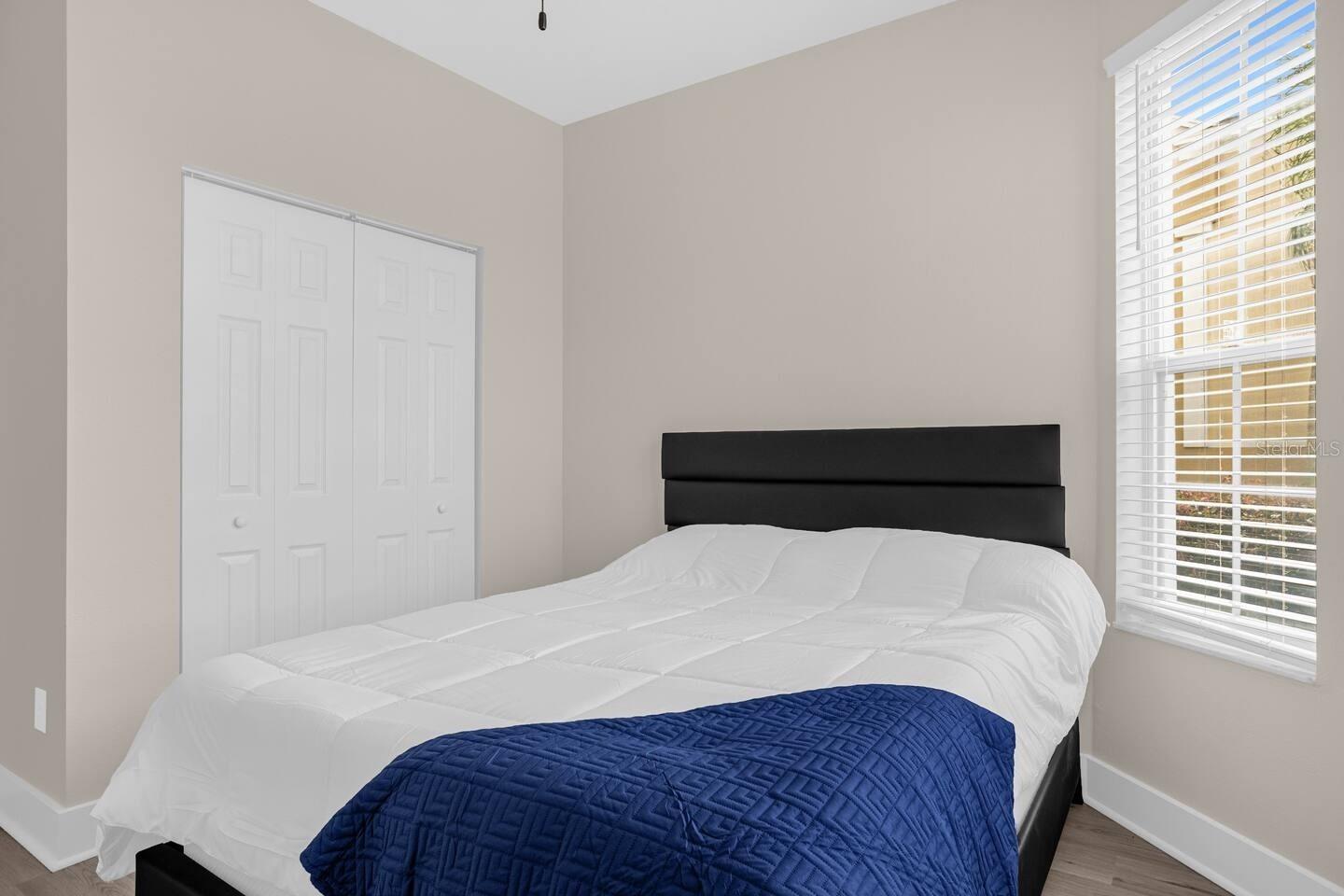 Bedroom with a black headboard, white bedding, navy quilt, and window with blinds.