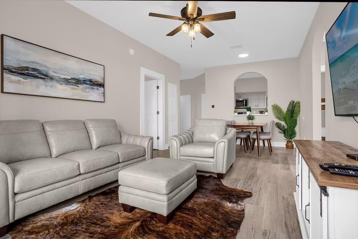 Furnished living room with gray leather seating, a dark rug, and an open dining area and kitchen.