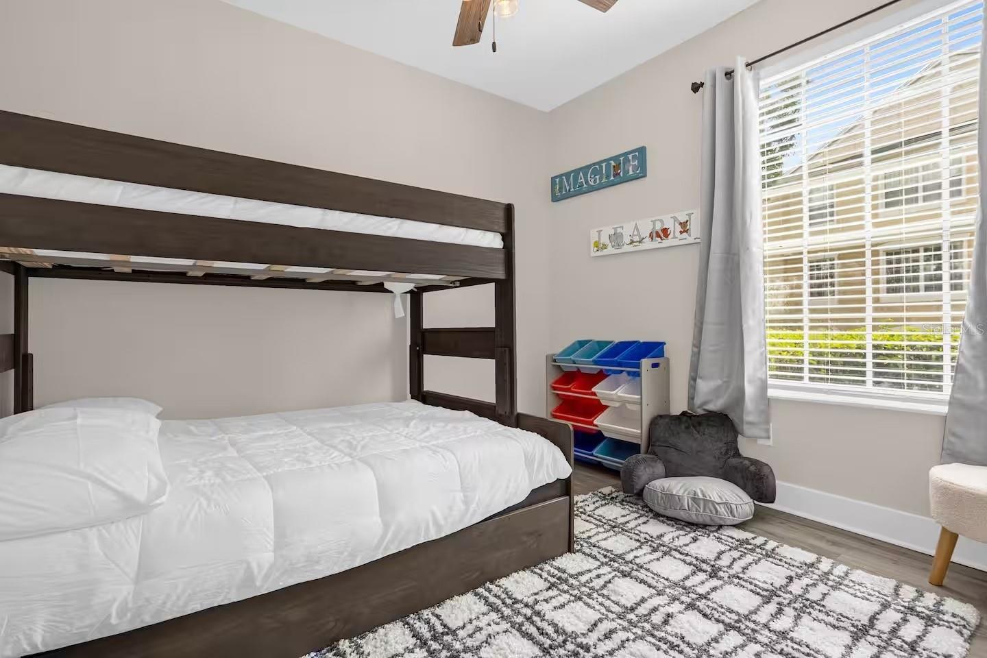 Bedroom with a dark wood bunk bed, colorful storage bins, and a large window with white blinds.
