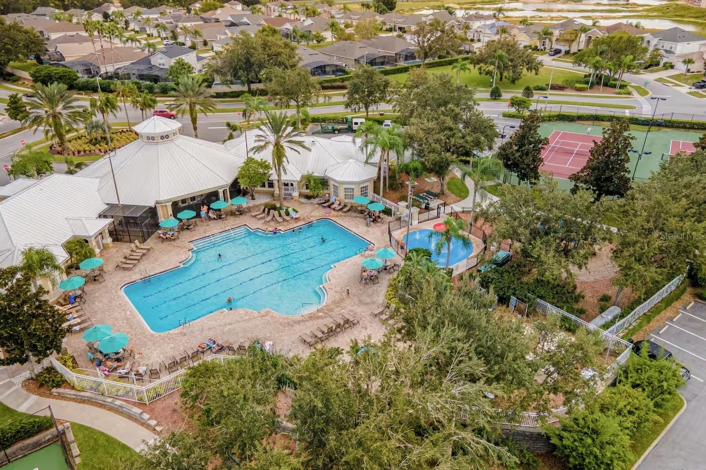 Community swimming pool and clubhouse with tennis courts and palm trees.
