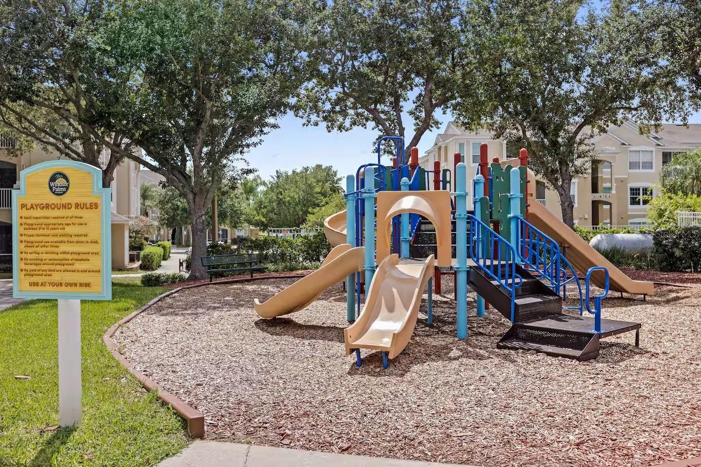Resort playground with colorful slides and climbing equipment beside a playground rules sign.