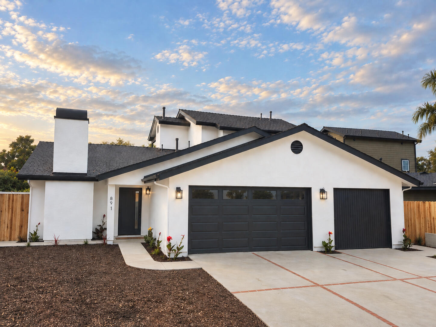 White stucco home with dark trim, two garage doors, and a broad paved driveway at golden hour.