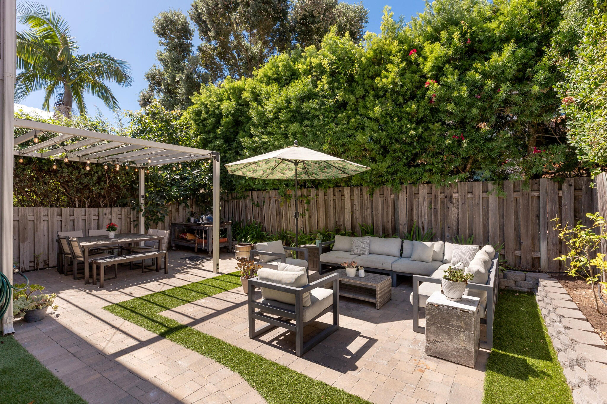 Furnished backyard patio with a pergola dining area and cushioned lounge seating beneath a large umbrella.