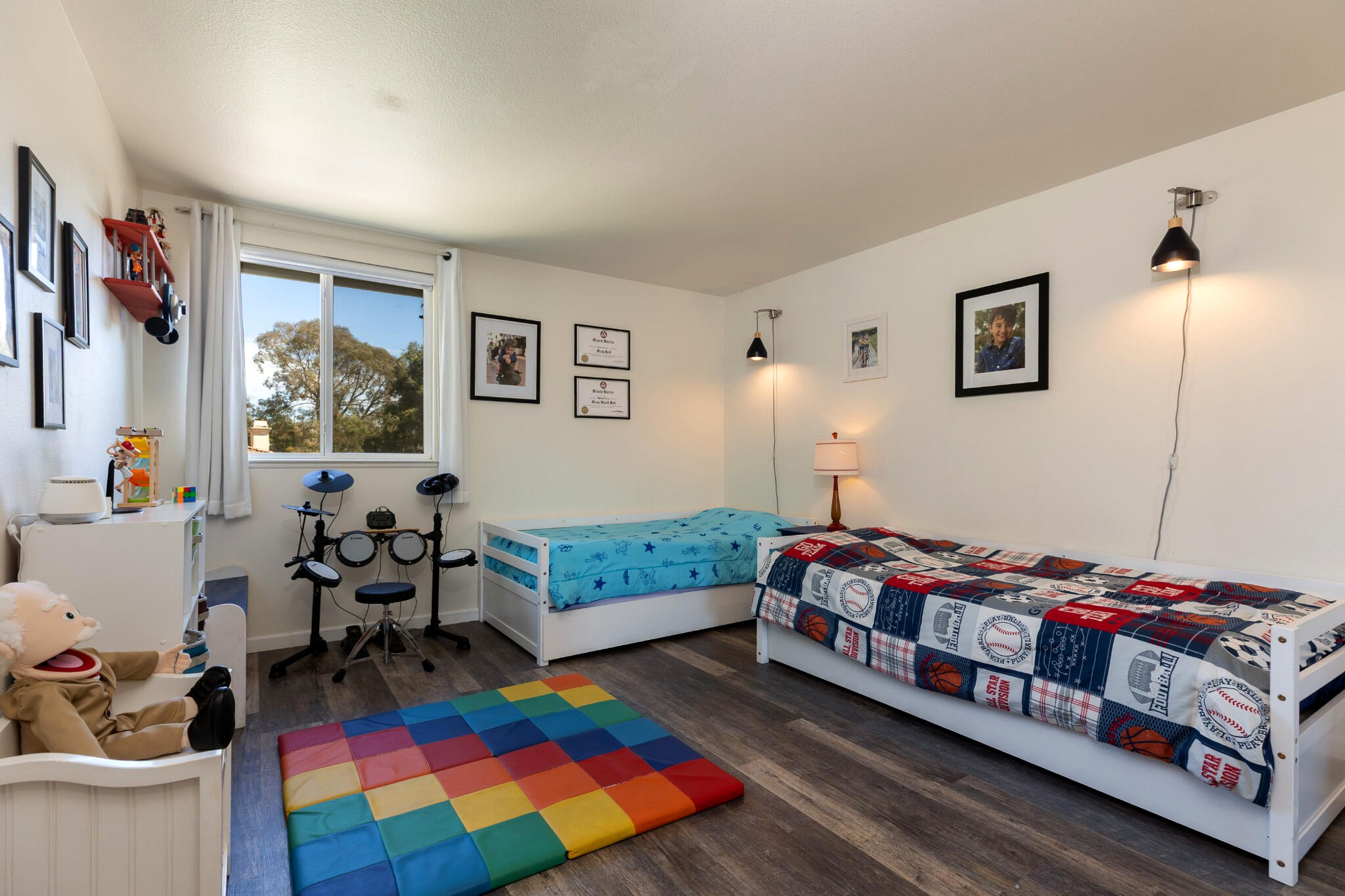 Bedroom with two single beds, a colorful play mat, and an electronic drum kit.