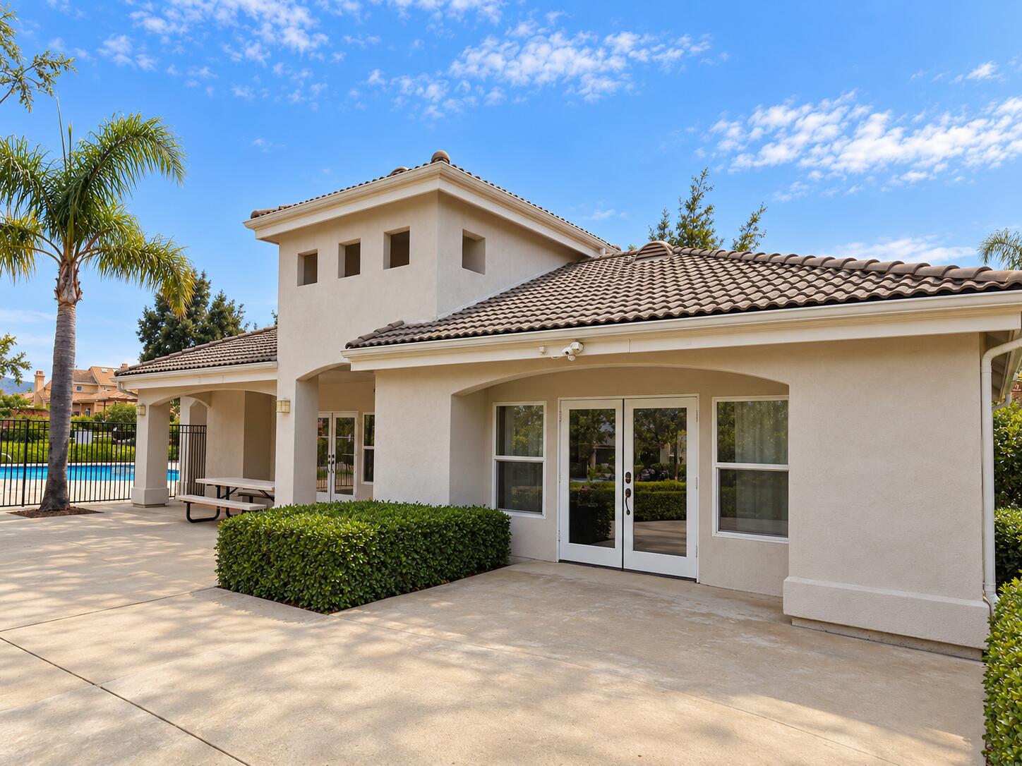 Rear exterior of a stucco home with a covered patio, tiled roof, and fenced swimming pool.