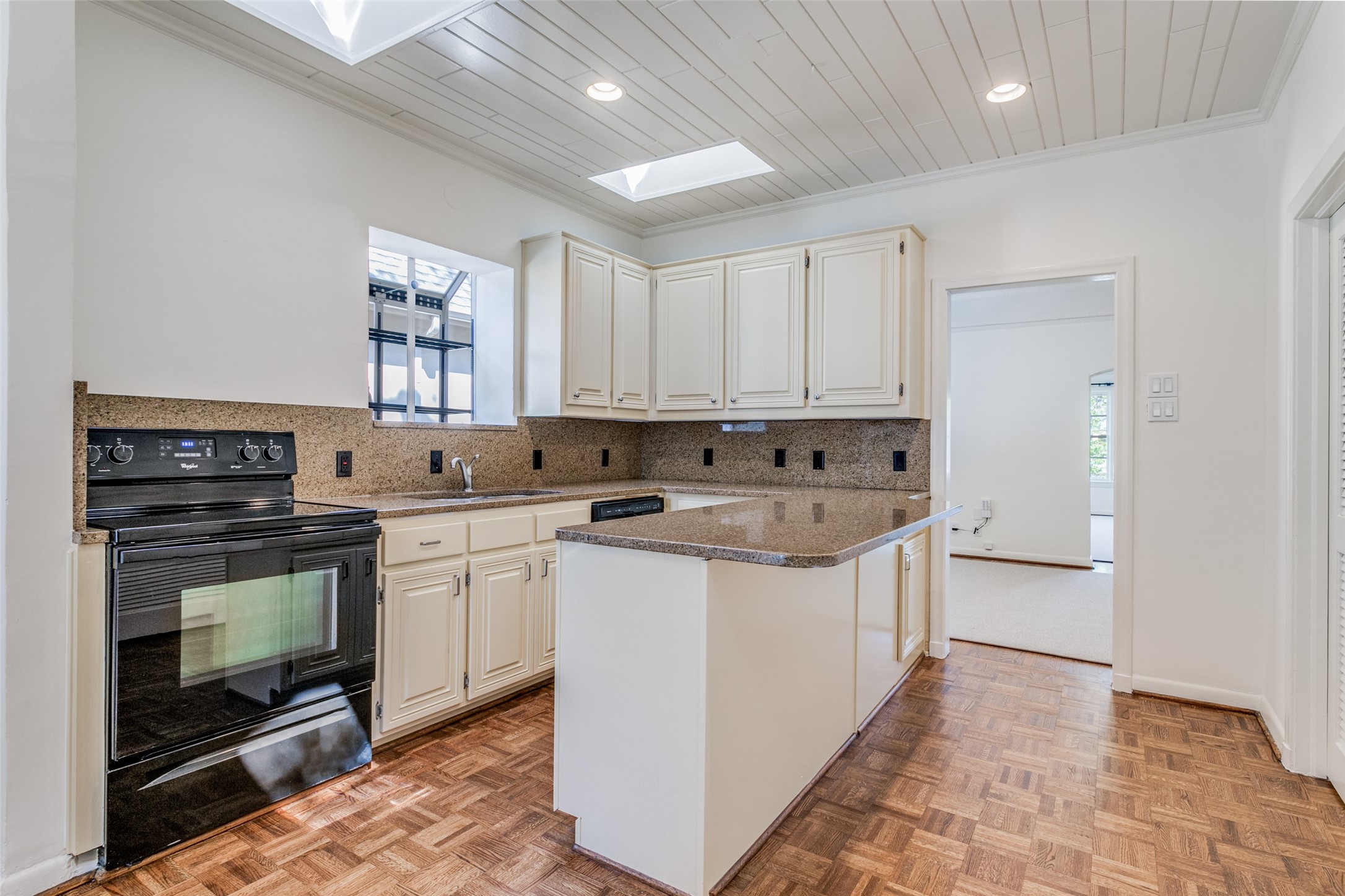 Kitchen with a central stone-topped island, cream cabinets, and parquet flooring.