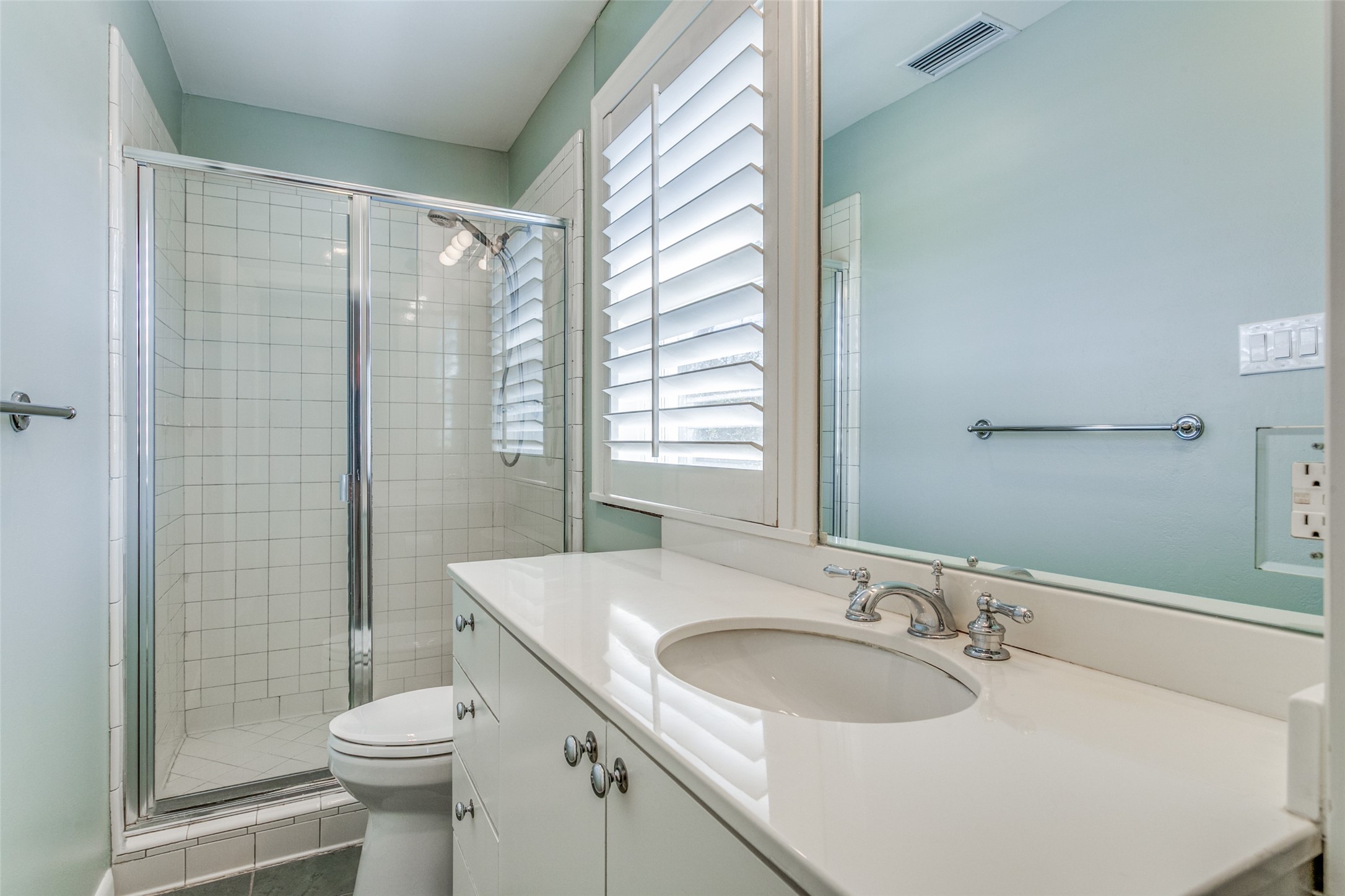 Bathroom with a white vanity and tiled glass shower beside a shuttered window.