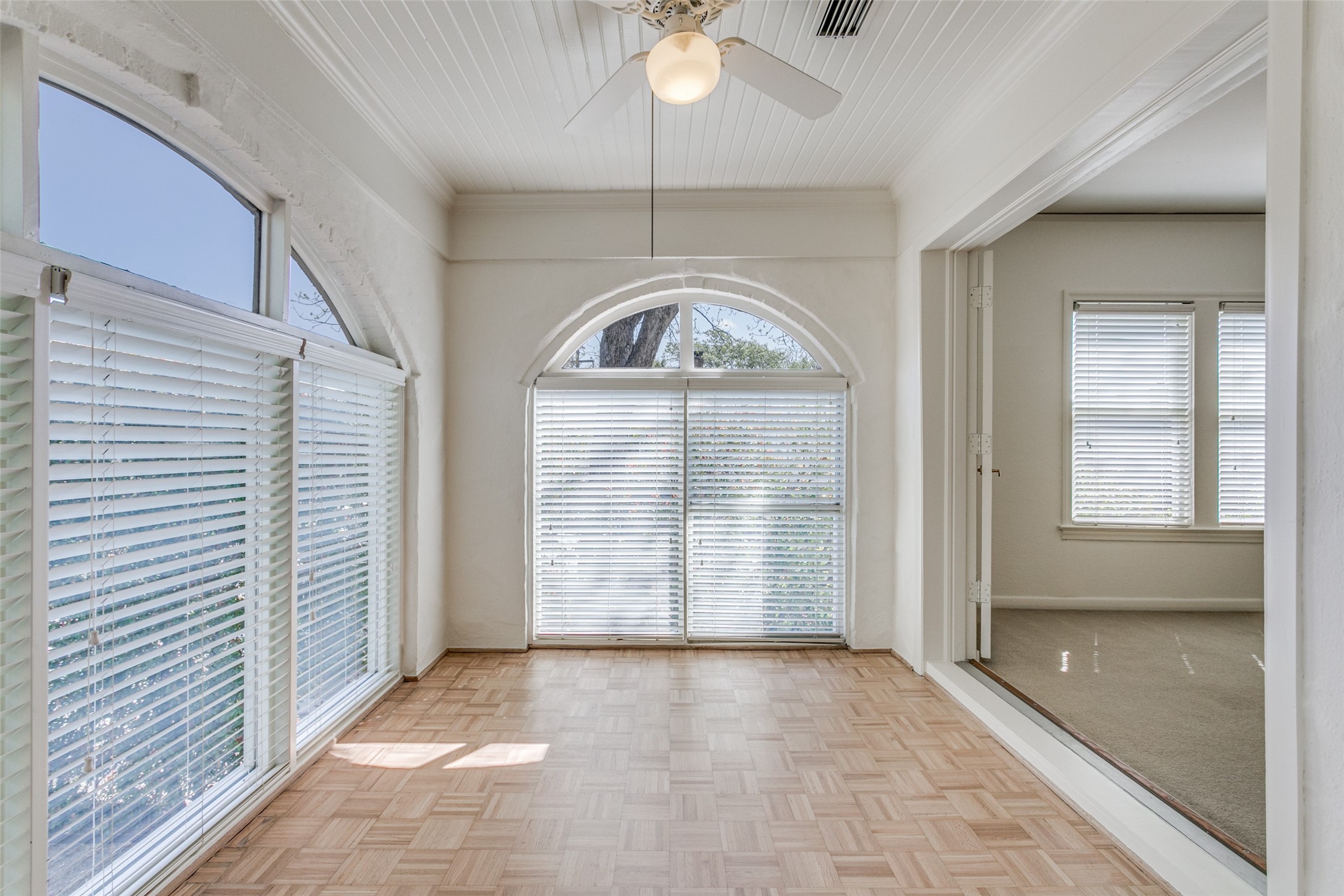 Vacant sunroom with parquet flooring, arched windows, and a ceiling fan.