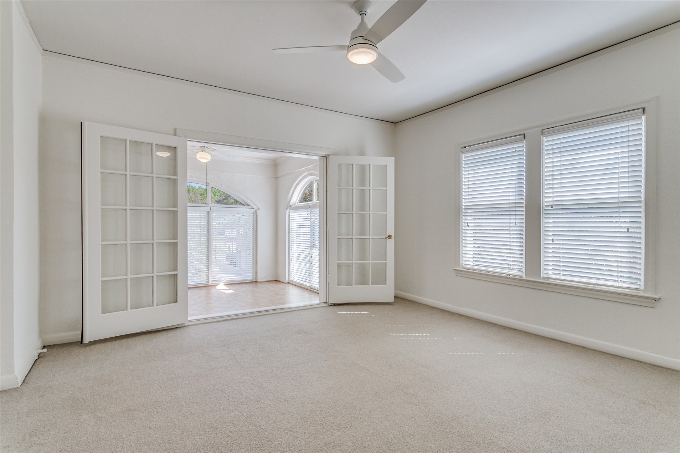 Unfurnished carpeted room with French doors opening to a bright sunroom and windows with blinds.