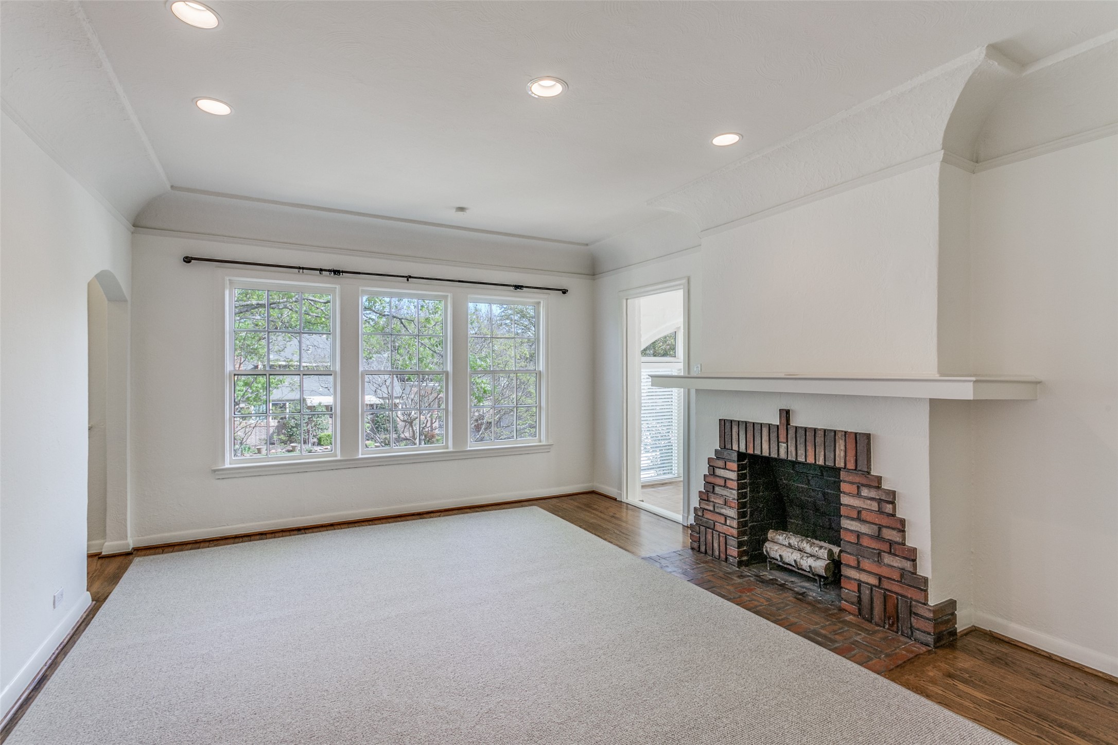 Empty living room with three large windows and a brick fireplace with a wide mantel.