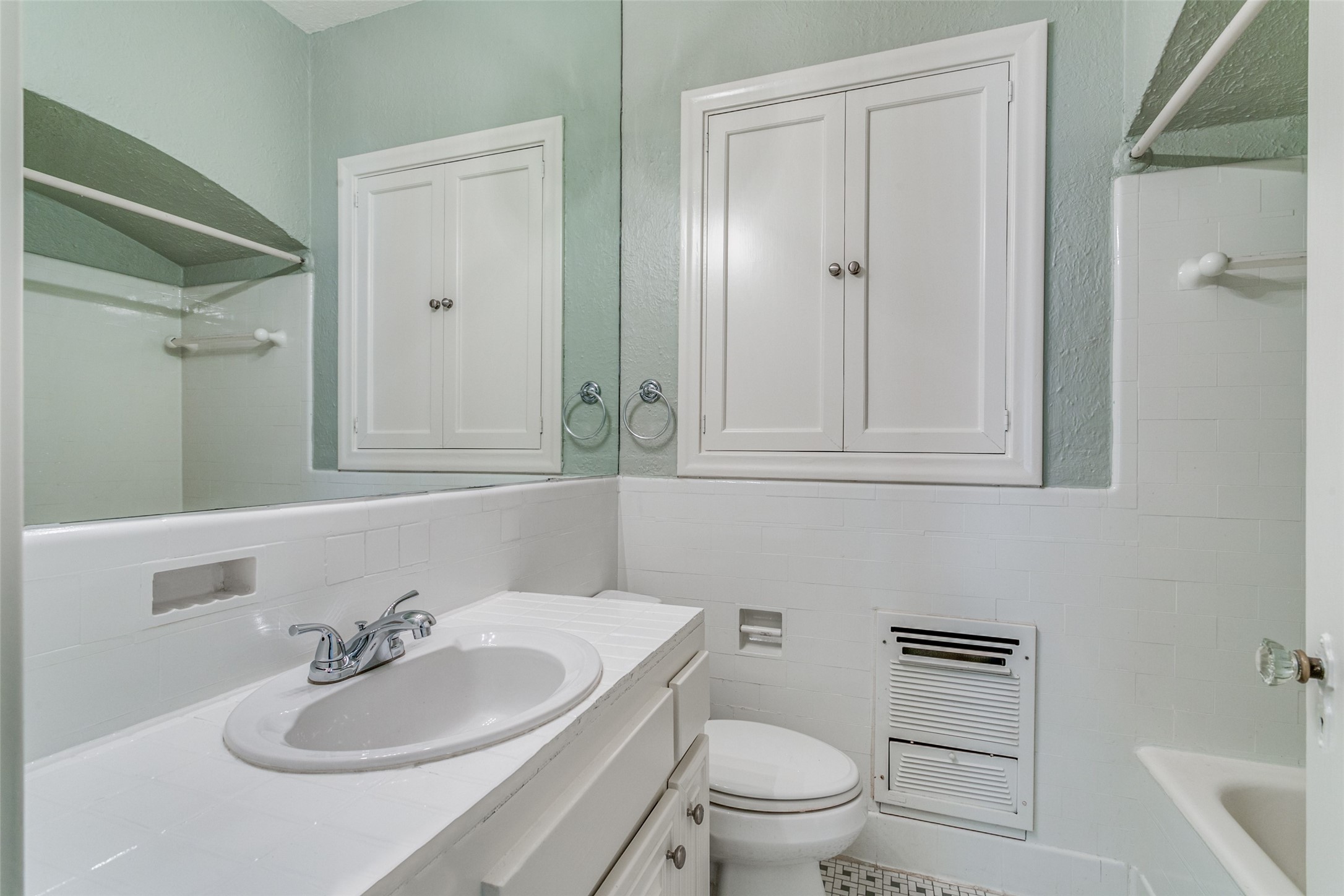 Bathroom with a tiled vanity, mirrored cabinets, toilet, and pale green walls.