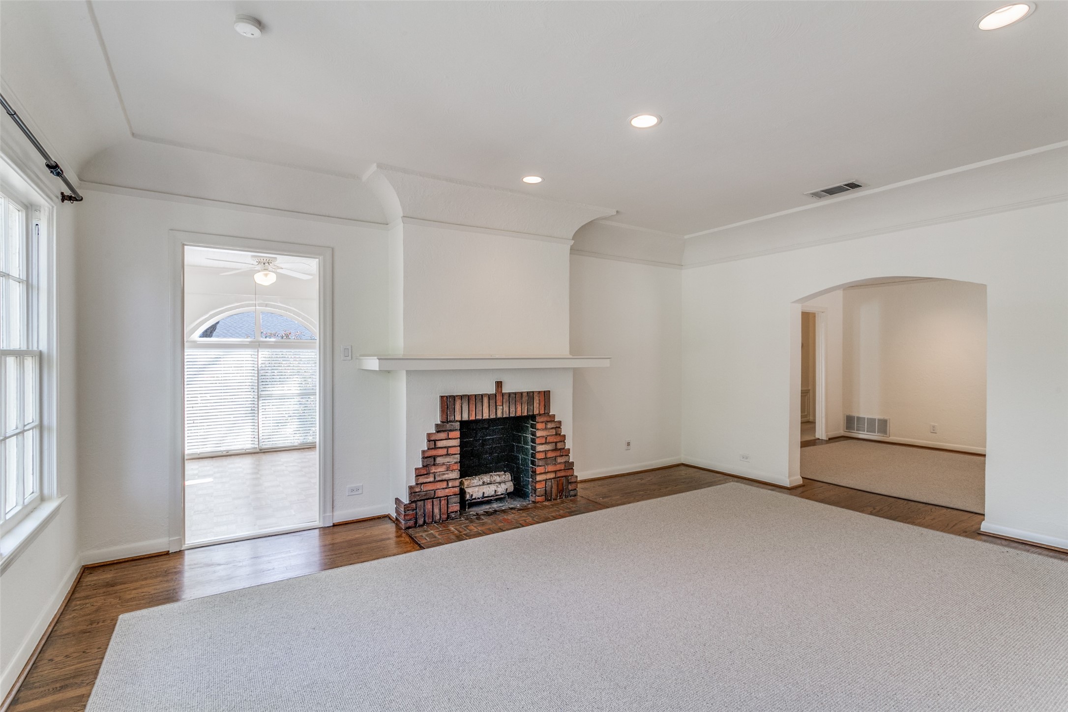 Unfurnished living room with a brick fireplace, tall windows, and an arched opening to an adjoining room.