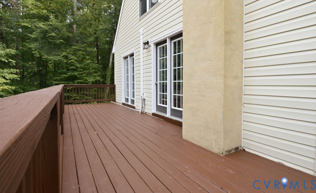Raised brown deck beside a light-sided house, with French doors and leafy trees beyond.