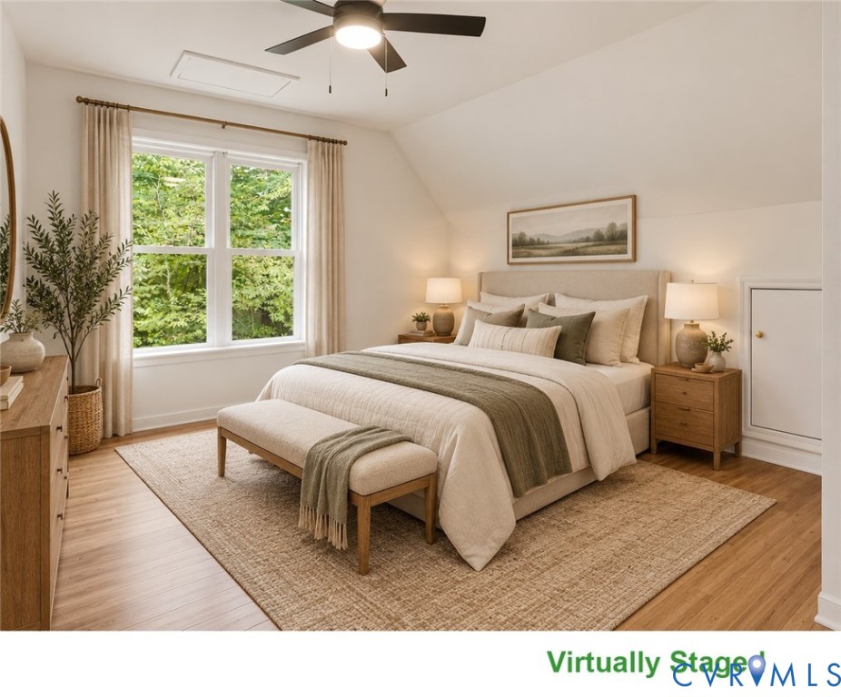 Staged bedroom with a large bed, upholstered bench, and leafy views through a window.