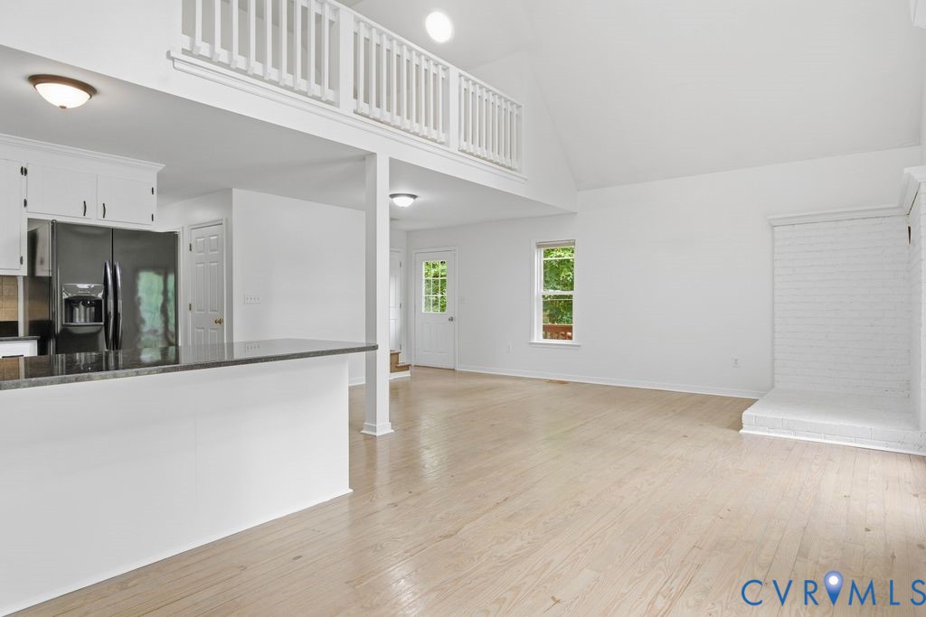 Open living room with light wood floors, a white brick fireplace, and a loft railing.