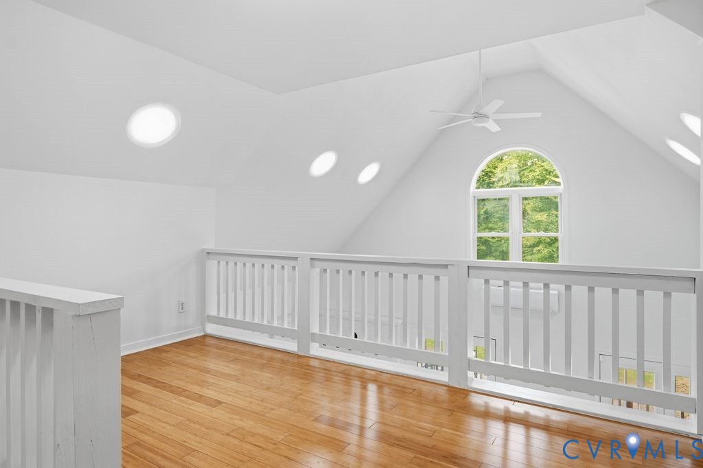 Upstairs loft with hardwood floors, white railings, and an arched window overlooking trees.