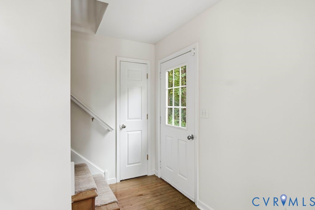 Entry hall with a windowed front door, staircase, upholstered bench, and wood flooring.