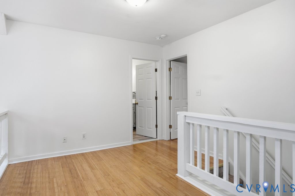 Upstairs landing with hardwood floors, two open doors, and a white stair railing.
