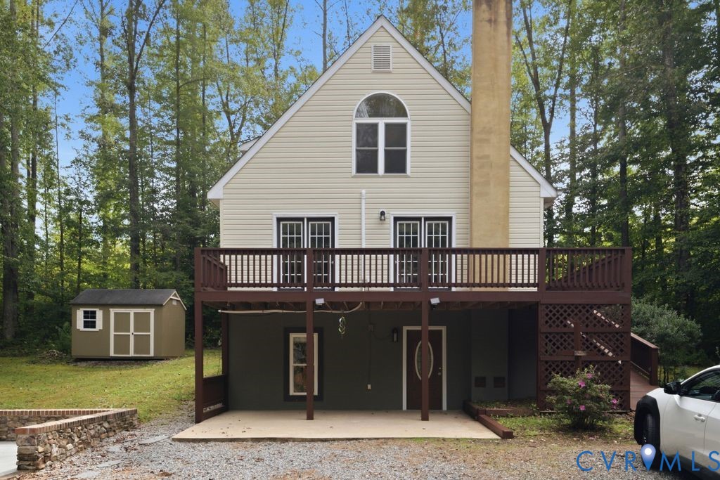Beige gabled house with a raised deck and covered patio, surrounded by trees.
