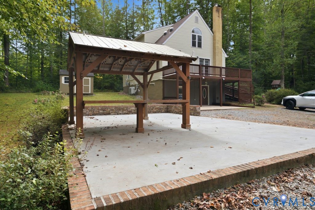 Two-story house with raised deck and large carport in a wooded setting.