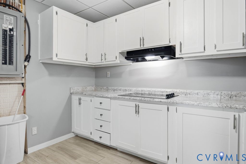 Kitchen with white cabinets, speckled countertops, and a black range hood.