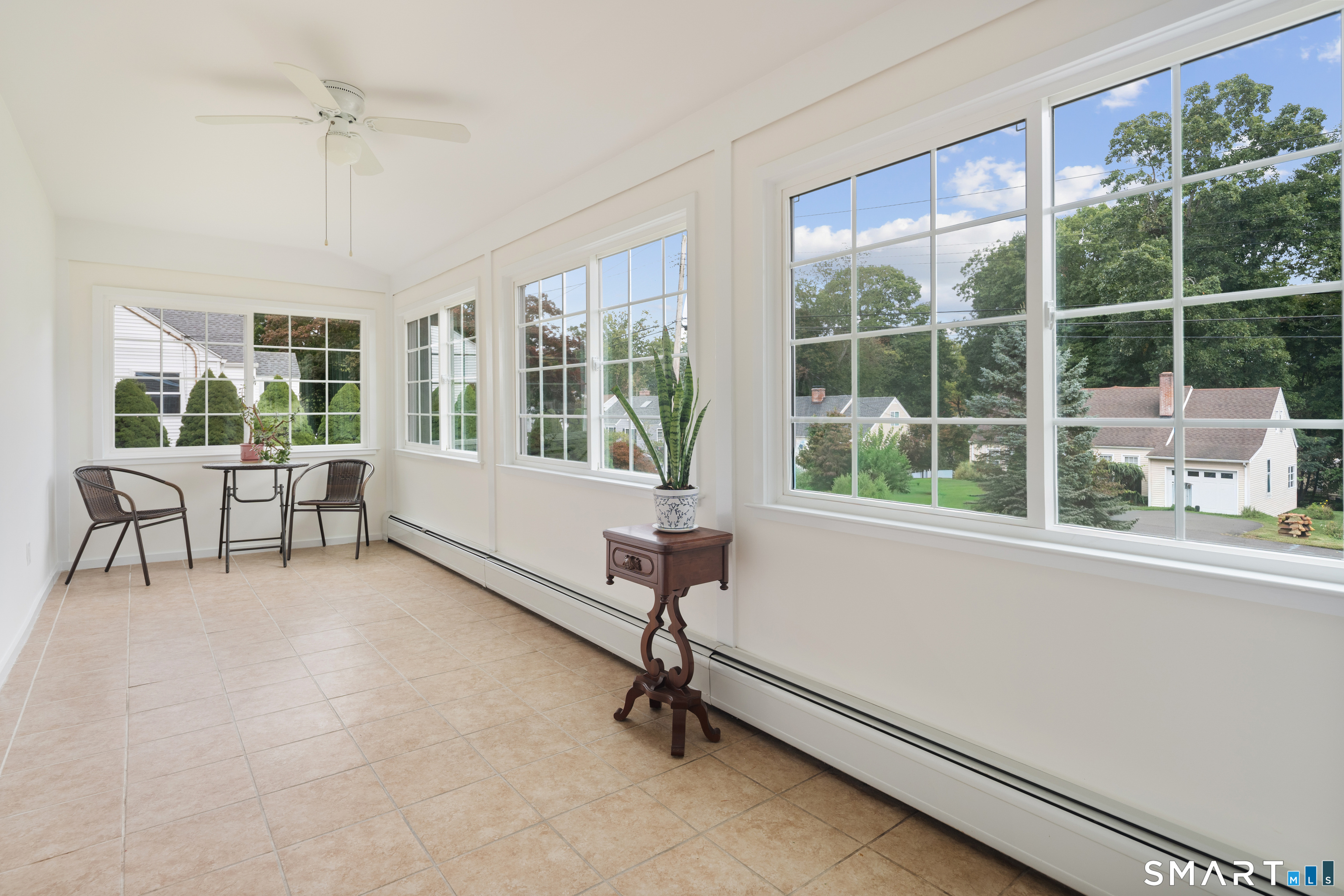 Bright sunroom with large windows, beige tile floors, and a small seating area.