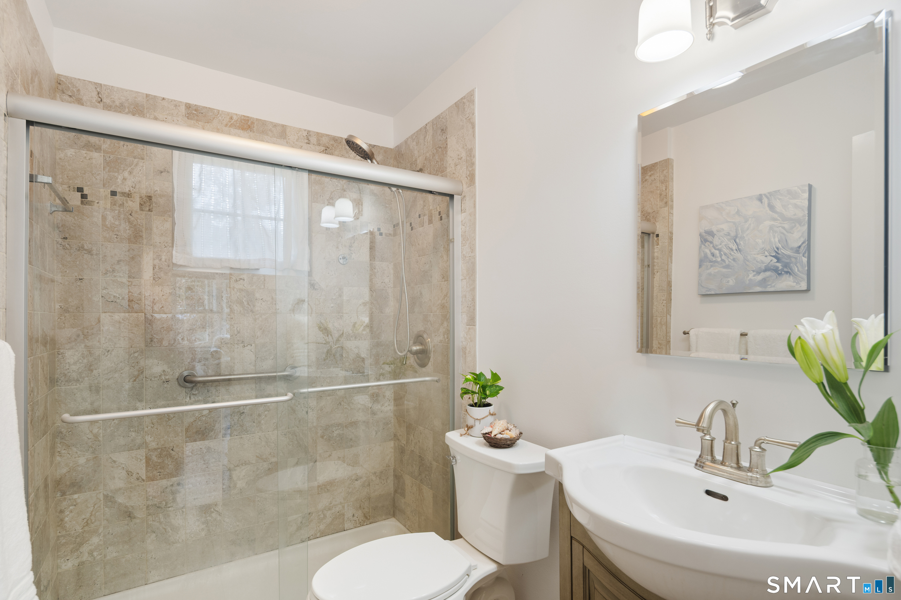 Bathroom with a beige tiled walk-in shower, glass doors, grab bars, and a white sink vanity.