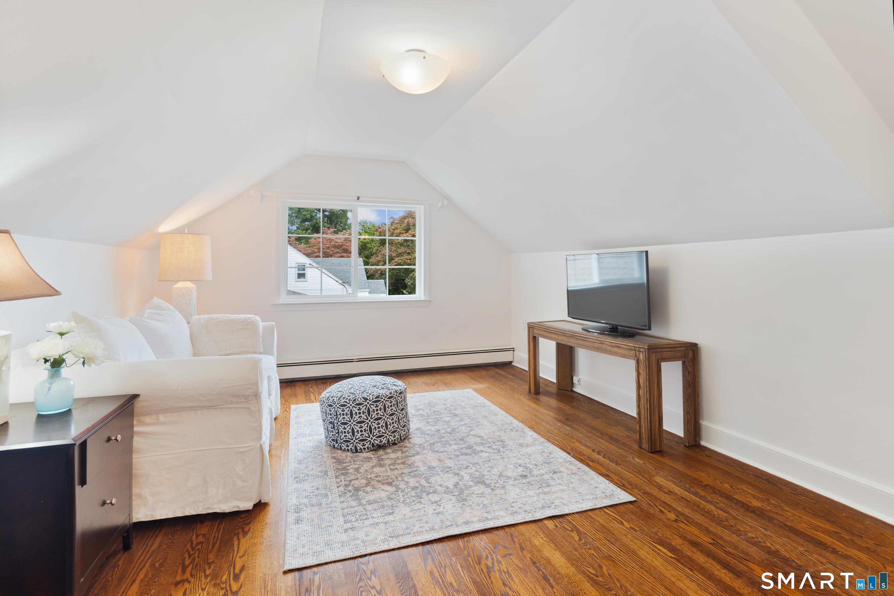 Sitting room with a sloped ceiling, hardwood floors, white sofa, and TV console.