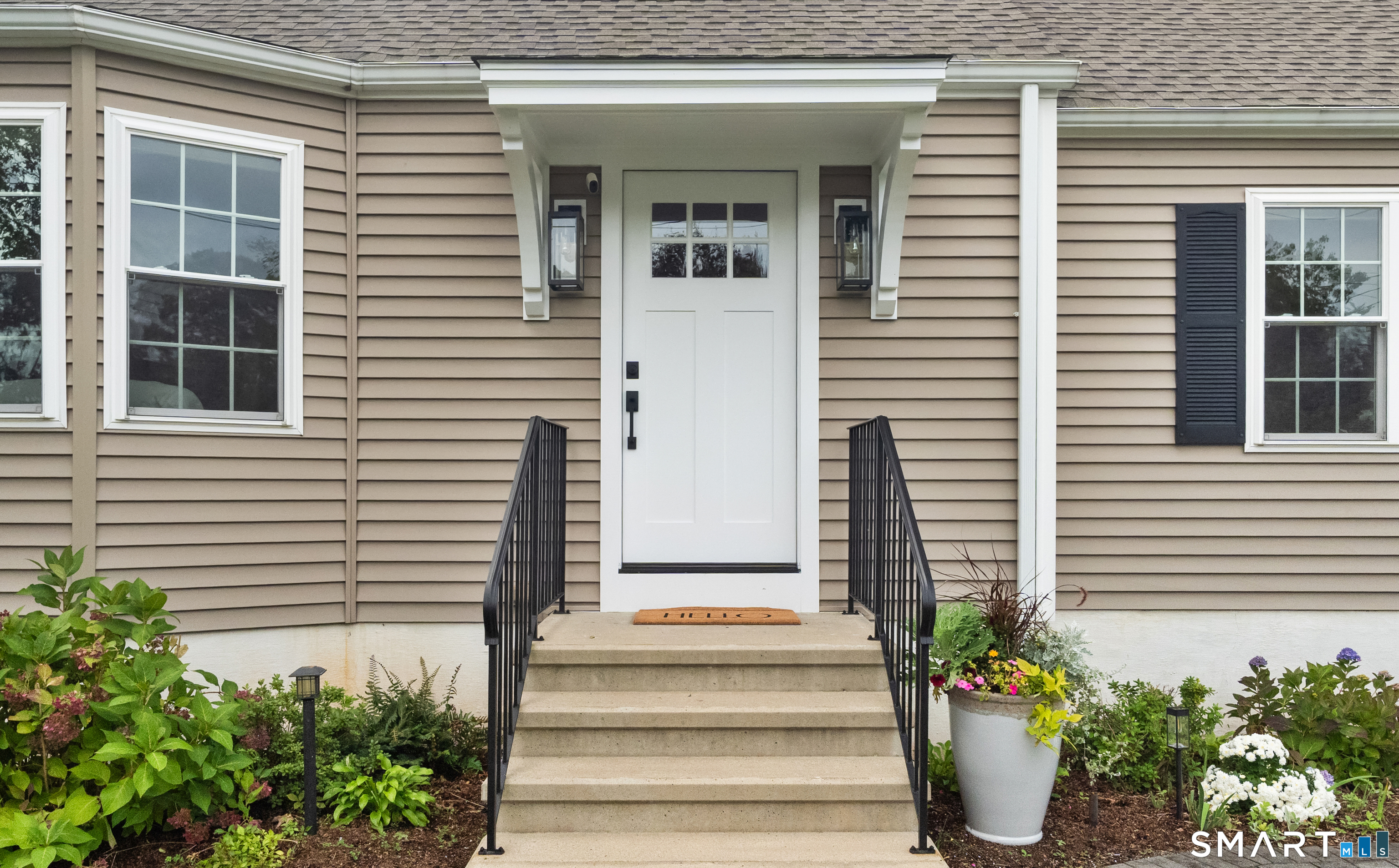 Home entrance with a white door, black stair railings, and flower beds.