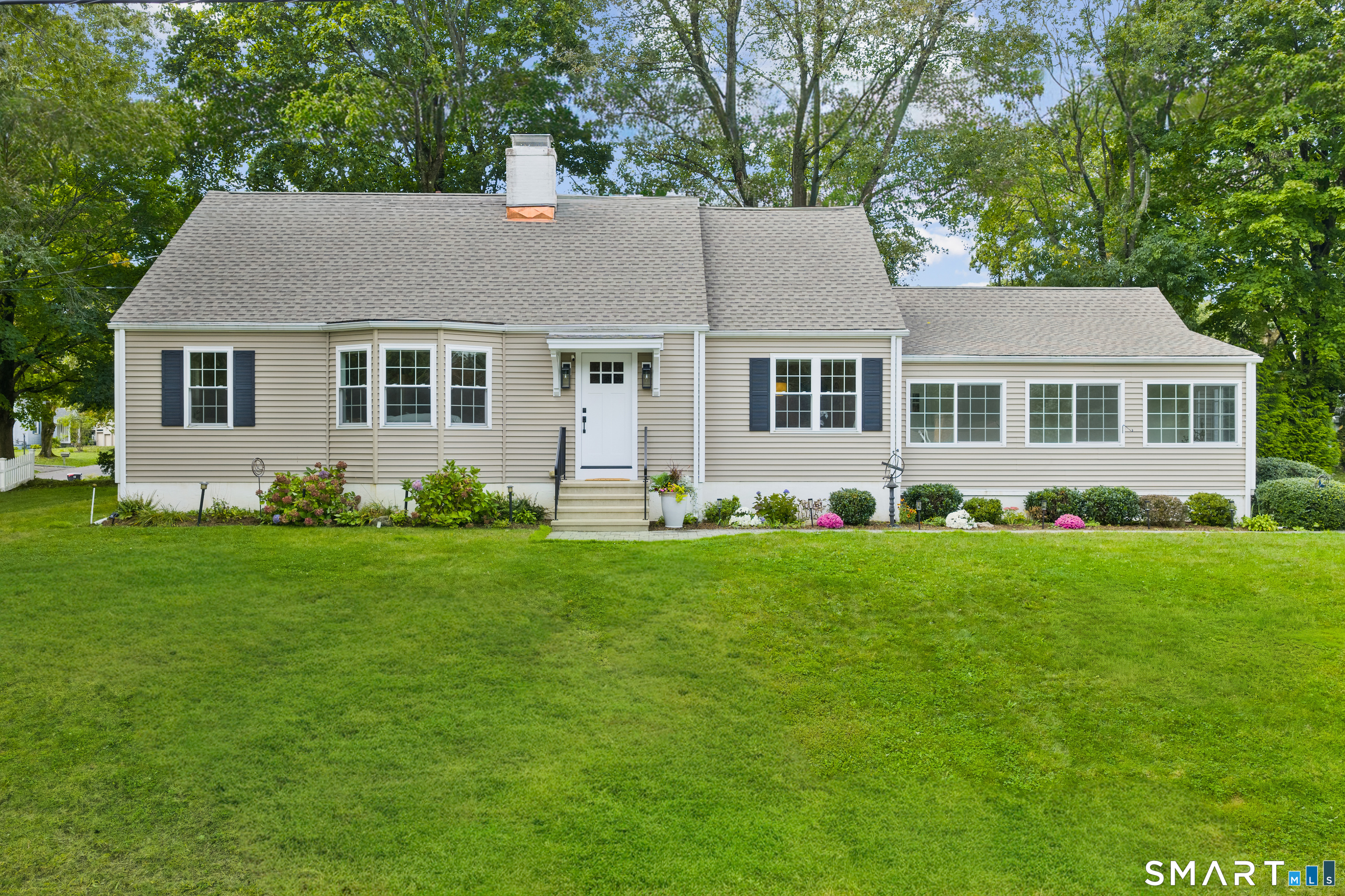 Beige ranch house with a broad green lawn, flower beds, and mature trees.