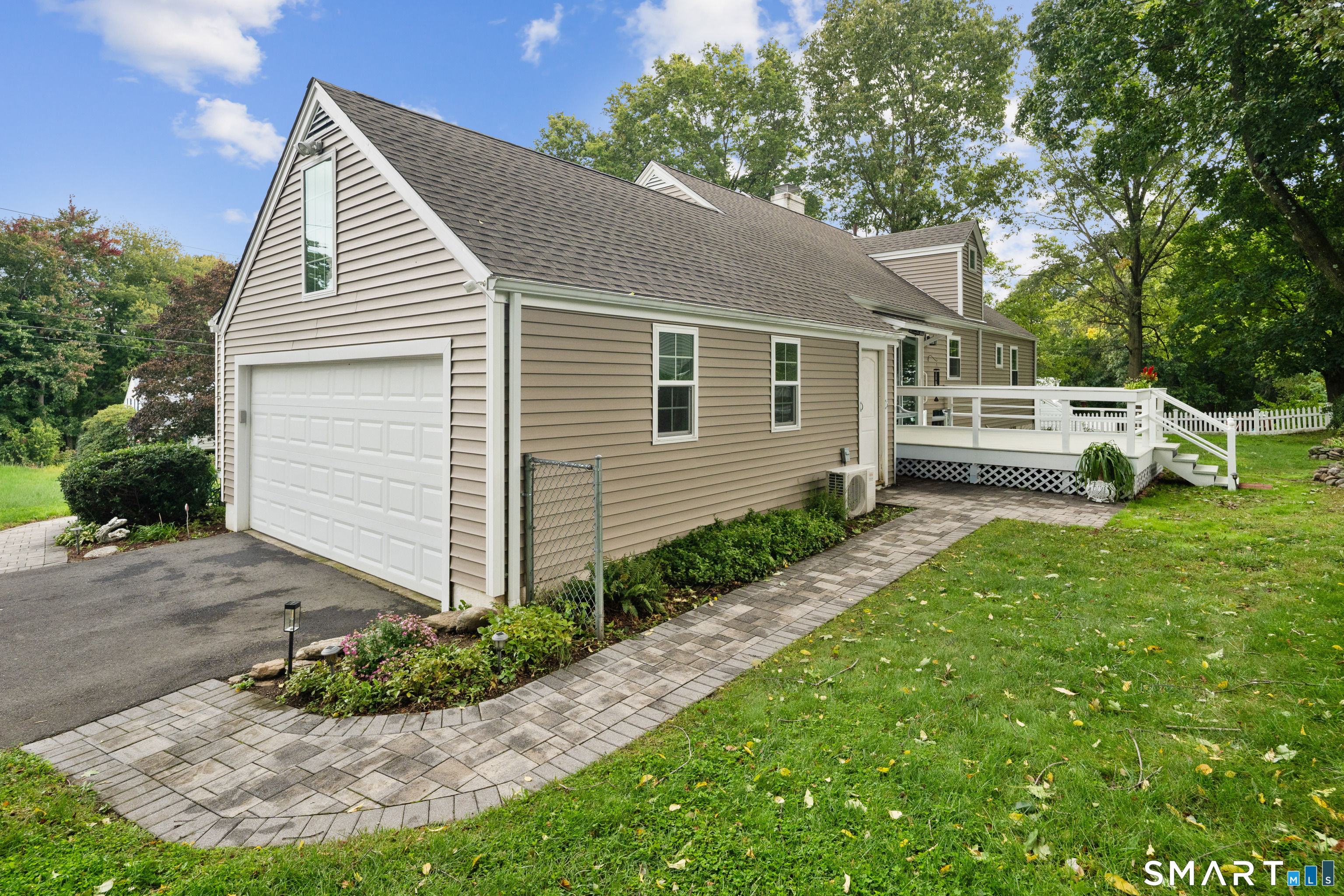 House exterior with a white garage, raised deck, and curved paver walkway.